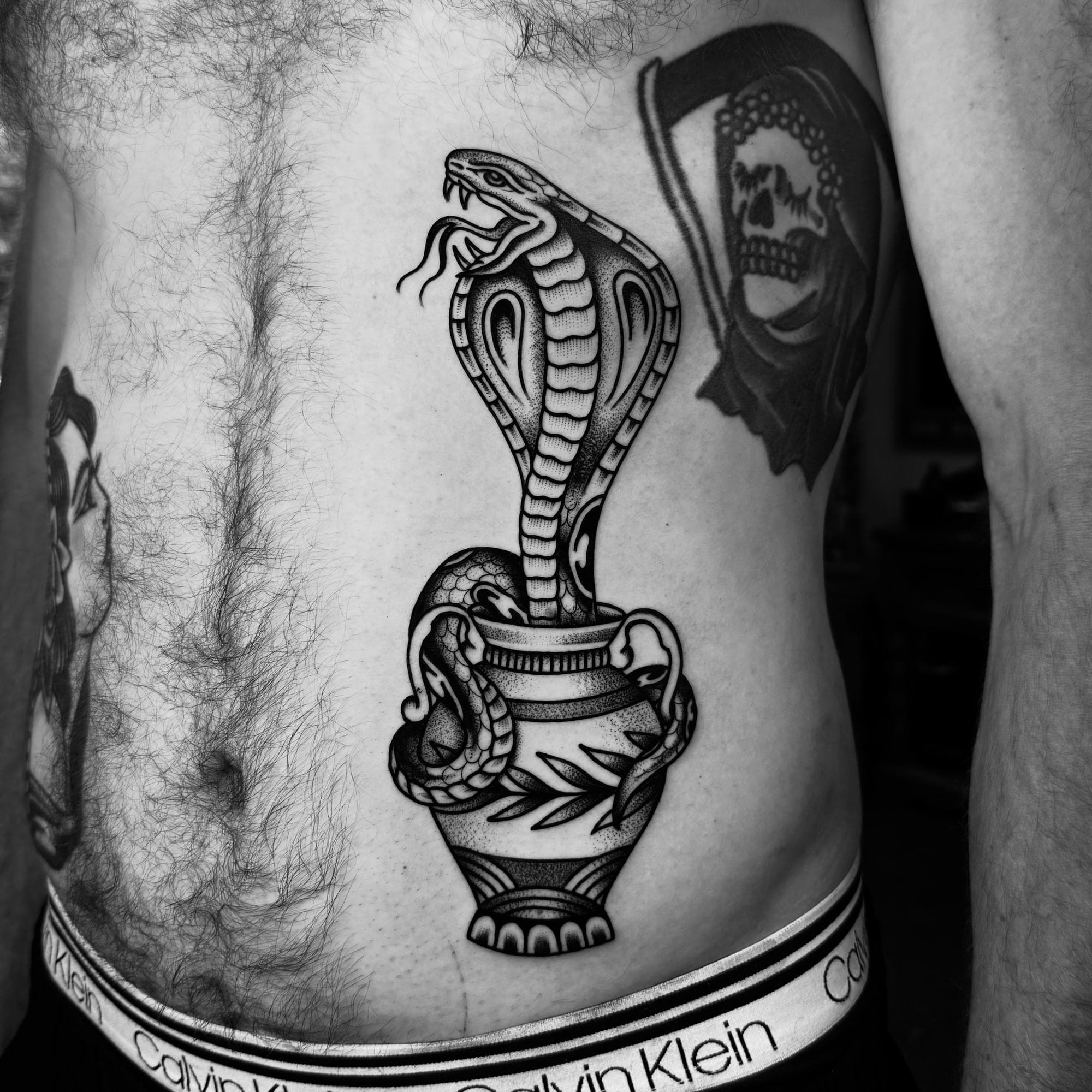 Tatouage traditionnel noir et gris d’un cobra sortant d’un vase